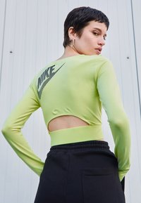 Hosszú ujjú lime zöld crop top, kivágott hátrésze van, és a bal felső részen fekete Nike logó található. Puha anyag és testhez simuló fazon.