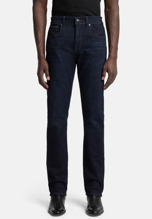 Dark blue denim jeans with a straight leg fit, five-pocket design, and subtle stitching details. Worn with black shoes and a black top.