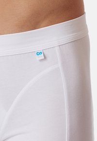 Weiße Baumwoll-Boxershorts mit einem bequemen elastischen Bund und einem kleinen blauen Stoffetikett mit einem Logo auf der Vorderseite.