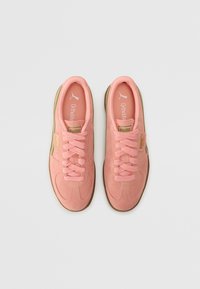 Baskets en daim rose clair avec des accents texturés, bout rond, lacets plats et semelle en caoutchouc marron. Présentent un logo sur le côté et la semelle intérieure.