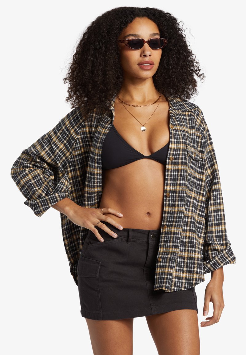 Sort og gulternet skjorte med åbne knapper over en sort bikini-top, parret med en sort mini-nederdel. Har lange ærmer og en afslappet pasform.