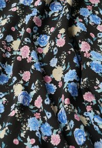 Tissu noir présentant un motif floral avec des fleurs roses, bleues et crème. La texture semble lisse, avec des plis et des drapés subtils.