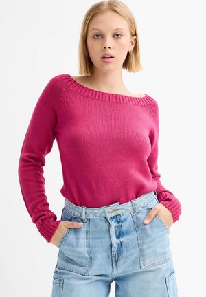 Suéter de punto fucsia con escote ancho y detalles de canalé, combinado con pantalones de mezclilla azul claro de talle alto. Mangas largas con puños ajustados.