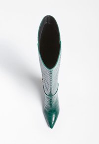 Bota de cuero verde con estampado de cocodrilo, con punta afilada, altura hasta la mitad de la pantorrilla y textura suave. Presenta un sutil acento cerca del tobillo.