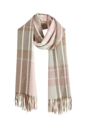 Ung kvinde iført en blå skjorte, beige jakke, sorte bukser og et stort lyserødt og beige ternet tørklæde mod en neutral baggrund.