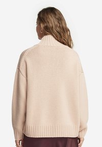 Jasnoróżowy sweter dzianinowy z wysokim kołnierzem, luźnym krojem, prążkowanym dołem i dużymi rękawami. Widoczny teksturowany wzór.