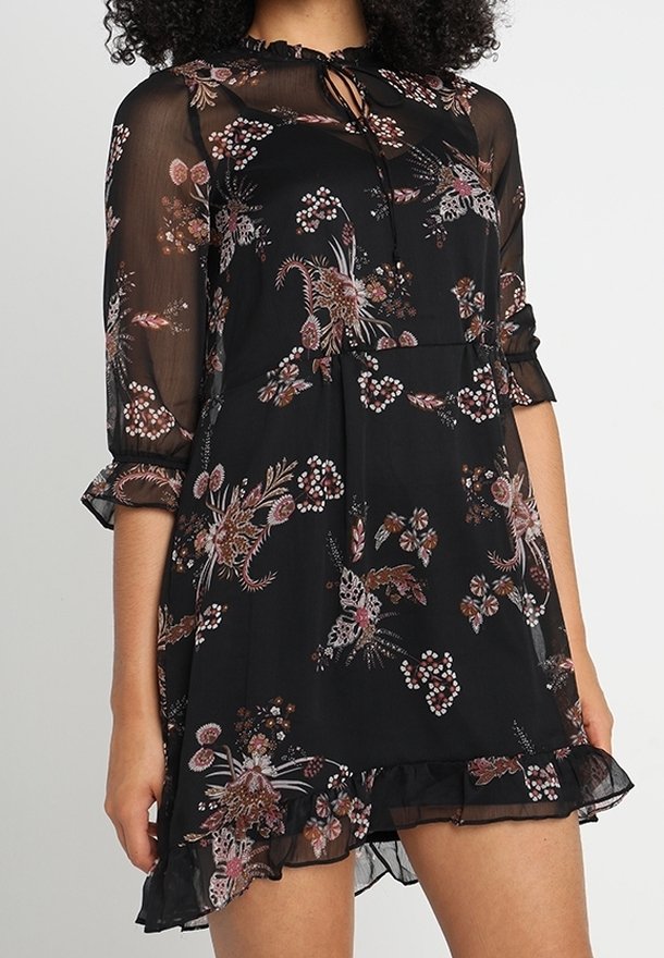 Robe noire transparente avec imprimé floral, manches trois-quarts, ourlet à volants et détail de col noué. Caractérisée par une texture légère et fluide.