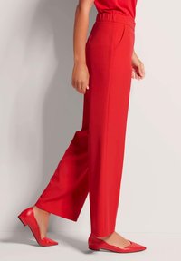 Rote, hoch taillierte Hosen mit geradem Bein, aus glattem Stoff. Kombiniert mit passenden roten, spitz zulaufenden Ballerinas.