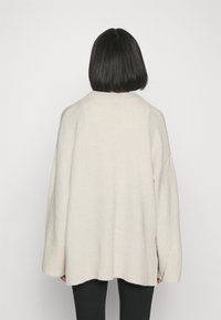 Överdimensionerad ljusbeige tröja, stickad textur, vida ärmar, ribbad nederkant, medellång bakdel, minimalistsik design, inga synliga mönster.