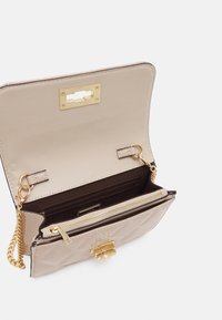 Prošívaná béžová kabelka s kultivováním, zlatými doplňky, řetízkovým popruhem a vnitřkem se dvěma přihrádkami, přičemž jedna z nich je uzavíratelná na zip.