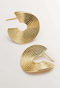 Pendientes de metal en tono dorado que presentan un diseño concéntrico y ondulado. Cada pendiente tiene un corte circular y una textura suave y brillante.