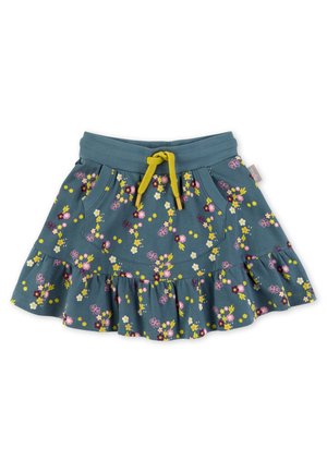 Gul bluse med lange ærmer og kattegrafik, kombineret med et blåt, lagdelt blomsterprintet nederdel. Hvide sneakers båret med lyserøde strømpebukser.