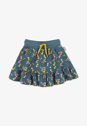 Haut à manches longues jaune avec un motif de chat, associé à une jupe fleurie bleue à volants. Baskets blanches portées avec des collants roses clairs.