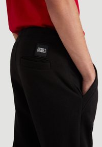 Sorte sweatpants med en baglomme, ribbet taljeelastik og et brandmærke-patch. Glat tekstur med diskrete sydetaljer.