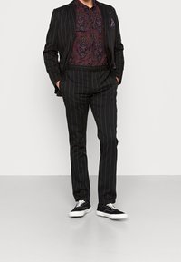 Black pinstriped suit jacket and trousers paired with a patterned purple shirt and black sneakers. Pocket square in the jacket's breast pocket.