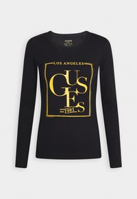 Černé tričko s dlouhým rukávem a žlutým textem "LOS ANGELES GUESS EST. 1981" uvnitř čtvercového rámečku na přední straně.