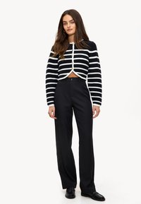 Cardigan cropped rayé en noir et blanc avec fermeture à boutons, associé à un pantalon noir taille haute et des mocassins noirs.