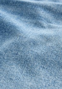 Svijetloplava denim tkanina s glatkom teksturom i suptilnim varijacijama boje. Vidljiv uzorak tkanja i mekani pada. Bez značajnih hardverskih ili ukrasnih detalja.