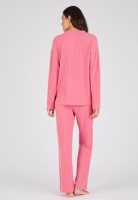 Conjunto de loungewear de color rosa con canalé que incluye una camiseta de manga larga y pantalones de corte relajado. El material parece suave con un acabado texturizado.