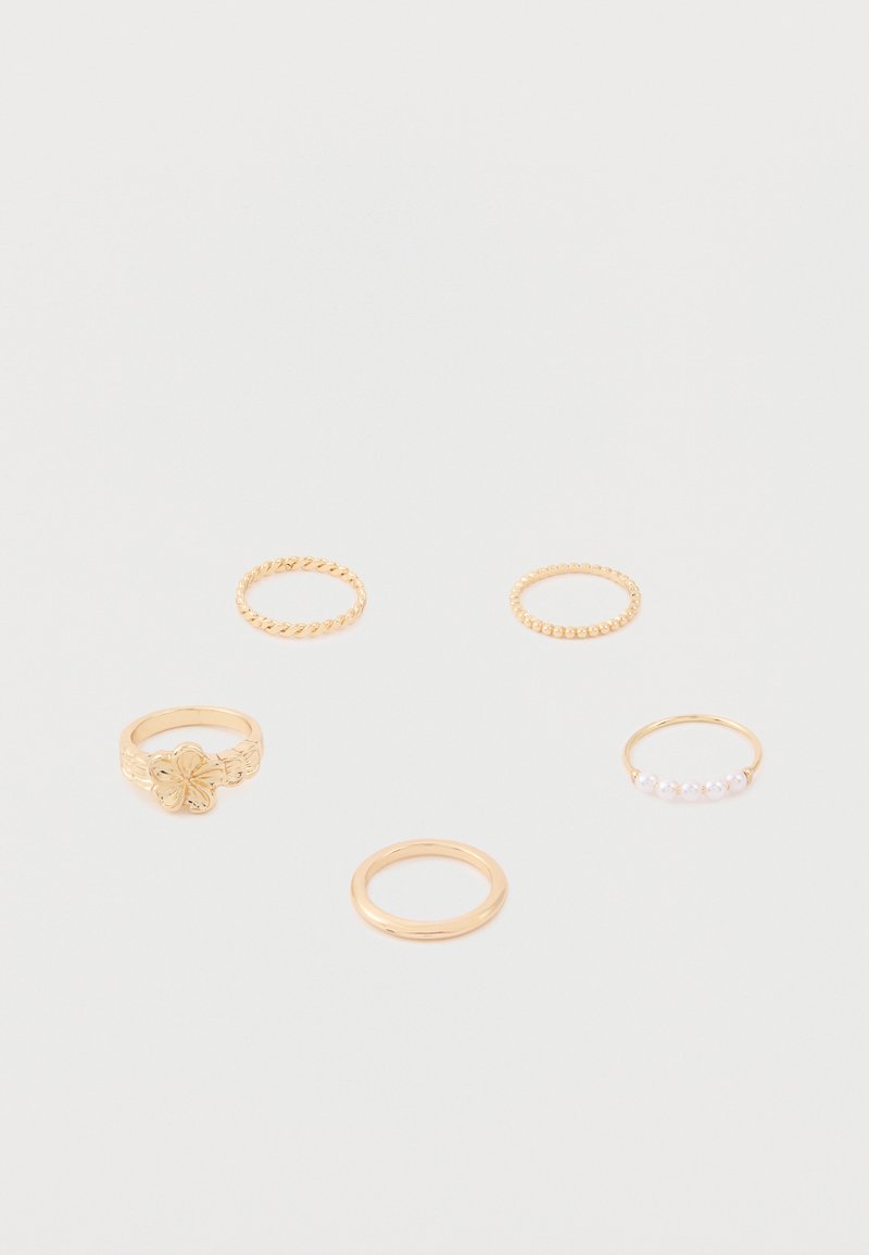 Πέντε χρυσά δαχτυλίδια σε λευκή επιφάνεια, περιλαμβανομένων ενός με ανθικό σχέδιο, ενός πλεκτού δαχτυλιδιού, ενός δαχτυλιδιού με χάντρες, ενός δαχτυλιδιού με μαργαριτάρια και ενός απλού δαχτυλιδιού.