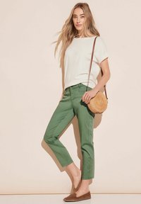 Vit kortärmad topp, gröna capribyxor, bruna slip-on skor och en rund halmhandväska med axelrem. Enkel, avslappnad outfit.