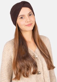 Un bandeau texturé marron avec un design torsadé, porté avec un cardigan en tricot crème comportant des accents de boutons dorés brillants.