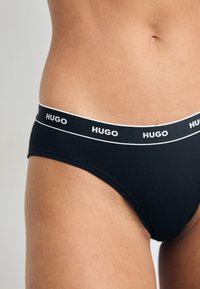 Boxeri negri din bumbac cu o bandă albă cu logo-ul care spune "HUGO", având o textură netedă și o croială joasă.