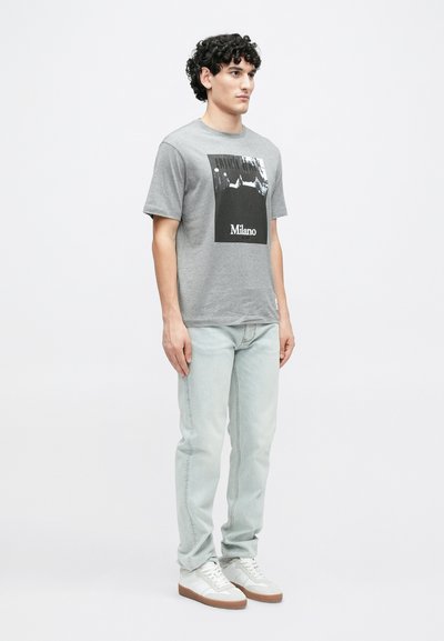 Γκρι βαμβακερό μπλουζάκι με μπροστινό σχέδιο σε ασπρόμαυρο με τη λέξη «Μιλάνο». Συνδυάζεται με ανοιχτόχρωμο τζιν και λευκά αθλητικά παπούτσια.