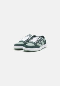 Green and mint suede sneakers with white laces and a textured surface. Features a rounded toe and thick rubber sole. Accented design elements.