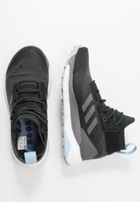 Par de zapatillas deportivas Adidas en negro y gris con suelas blancas, cordones y tiradores en azul claro, mostradas desde vistas superior y lateral sobre un fondo blanco.