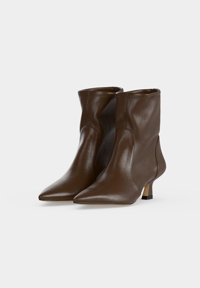 Paire de bottines en cuir marron à bout pointu avec petits talons kitten sur un fond clair uni.