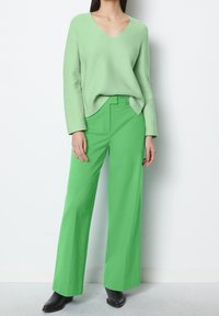 Light green v-neck sweater paired with bright green wide-leg pants. Both garments feature smooth textures, with a relaxed fit and modern design.