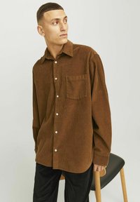 Chemise en velours côtelé marron avec un devant à boutons, des manches longues et une poche poitrine unique. Comprend des boutons blancs et une coupe décontractée.