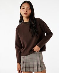Bruine gebreide trui met een ronde hals, gecombineerd met een geruite minirok in grijs, beige en rood, met plooien en een gestructureerde afwerking.