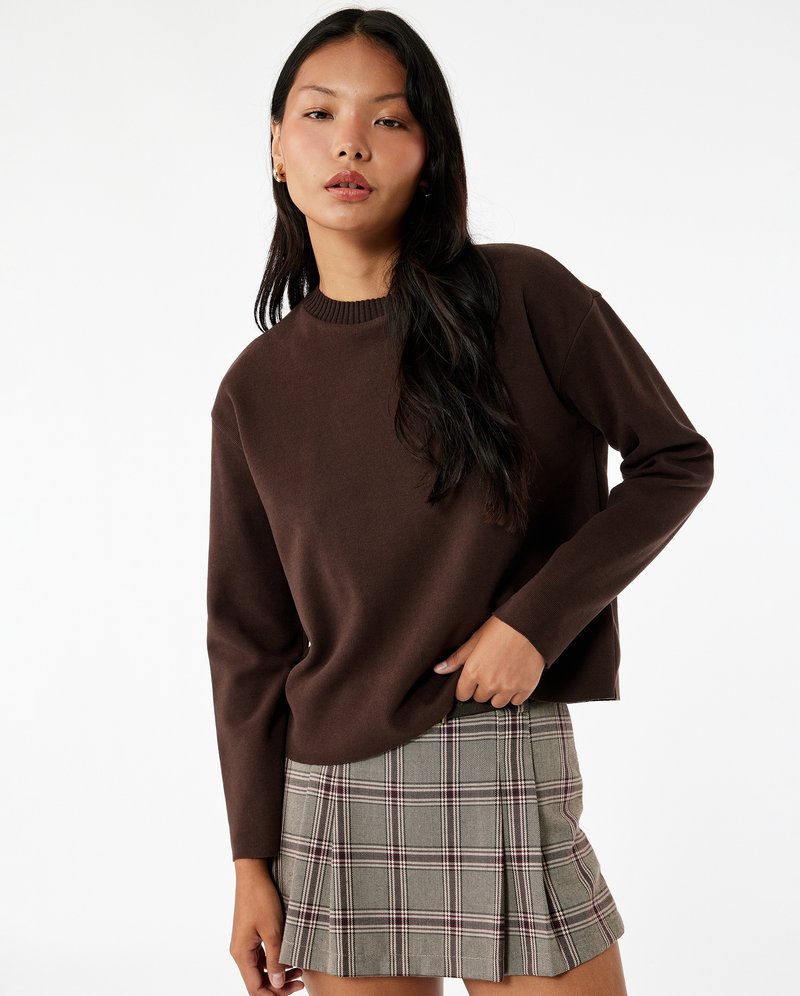 Bruine gebreide trui met een ronde hals, gecombineerd met een geruite minirok in grijs, beige en rood, met plooien en een gestructureerde afwerking.