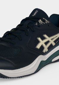 Σκούρο μπλε αθλητικό παπούτσι Asics με λευκό λογότυπο, μαύρα κορδόνια και λευκή και πράσινη απορροφητική σόλα, σχεδιασμένο για τρέξιμο ή προπόνηση.