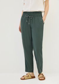 Dark green, lightweight, elastic-waist pants with drawstring detail and pockets, paired with brown woven sandals.