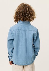 Μακρυμάνικο φωτεινό μπλε πουκάμισο από τζιν ύφασμα, με μανσέτες με κουμπιά, γιακά και πιέτες στην πλάτη. Λείο ύφασμα και άνετη εφαρμογή.