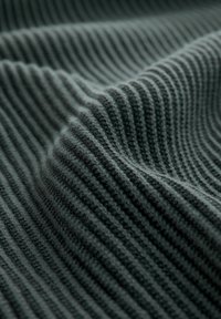 Tessuto a costine di un verde scuro con una texture morbida, che mostra onde e ombre textured, evidenziando la sua profondità e il suo pattern.