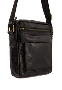 Černá kůže křížová taška s texturovaným povrchem, která má přední kapsu na zip, nastavitelný popruh a mosazné akcenty.