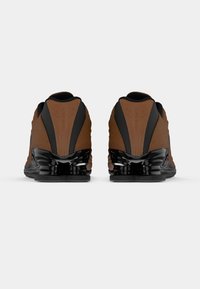 Παπούτσια Nike με καφέ υφή πάνω μέρος, μαύρες λεπτομέρειες και γυαλιστερή μαύρη σόλα από αφρό. Διαθέτουν στρογγυλεμένη φτέρνα και ομαλές καμπύλες.