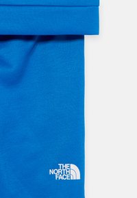 Μπλε βαμβακερό ύφασμα με λεία υφή, εμφανίζει το λευκό λογότυπο "The North Face" κοντά στο κάτω μέρος. Σχεδίαση με κυλιόμενο στρίφωμα.
