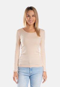 Beżowa dopasowana bluzka z długim rękawem i okrągłym dekoltem, o miękkiej teksturze i minimalistycznym wzornictwie. W połączeniu z jasnoniebieskimi dżinsami.