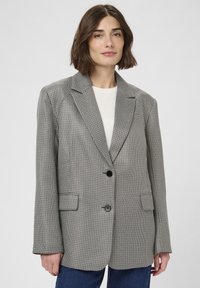 Šedý texturovaný blazer s klopovým límcem, zapínáním na jeden černý knoflík a dvěma předními kapsami. Nosit s bílým tričkem, které má volný střih.