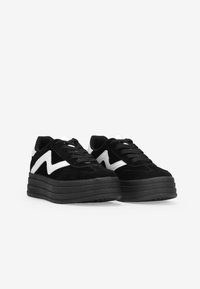 Zapatillas de plataforma de ante negro con una suela gruesa negra, que presentan franjas en zigzag blancas en los laterales y cordones blancos a juego.