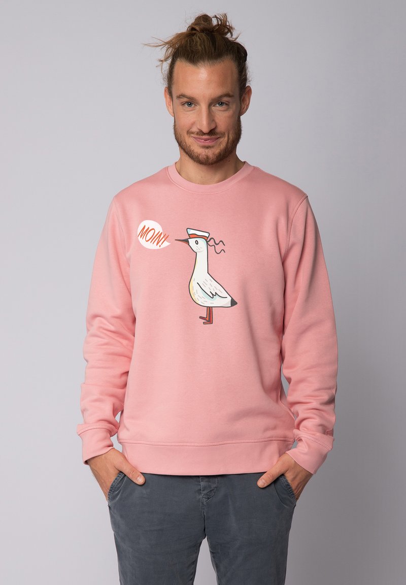 Roze sweatshirt met lange mouwen, met een cartoon vogelafbeelding en de tekst "MONN!" Super zachte stof, geribde mouwen en onderrand.