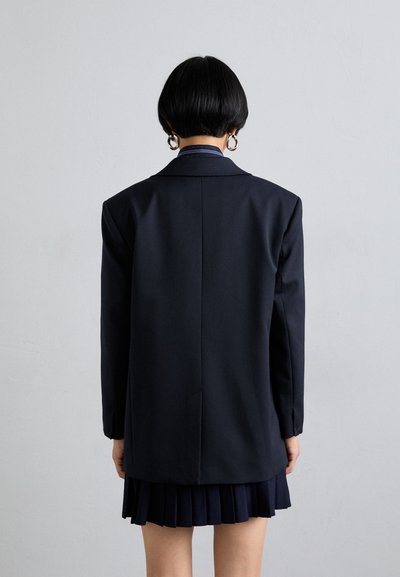 Navy-blauer Blazer mit geradem Rücken, strukturierten Schultern und glatter Textur, kombiniert mit einem plissierten navy-blauen Rock.