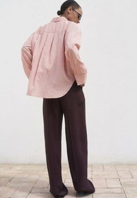 Chemise à boutons rayée rouge et blanche avec des manches surdimensionnées, associée à un pantalon brun foncé ample. Tissu lisse, silhouette décontractée.