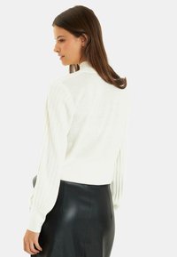 Witte ribgebreide trui met lange, gestructureerde mouwen, hoge hals, in combinatie met een zwarte leren rok, gladde textuur en aansluitend ontwerp.