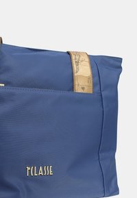 La borsa a spalla in nylon blu presenta una tracolla beige con un motivo a mappa e una tasca frontale; logo dorato 'T'Classe' nella parte inferiore.